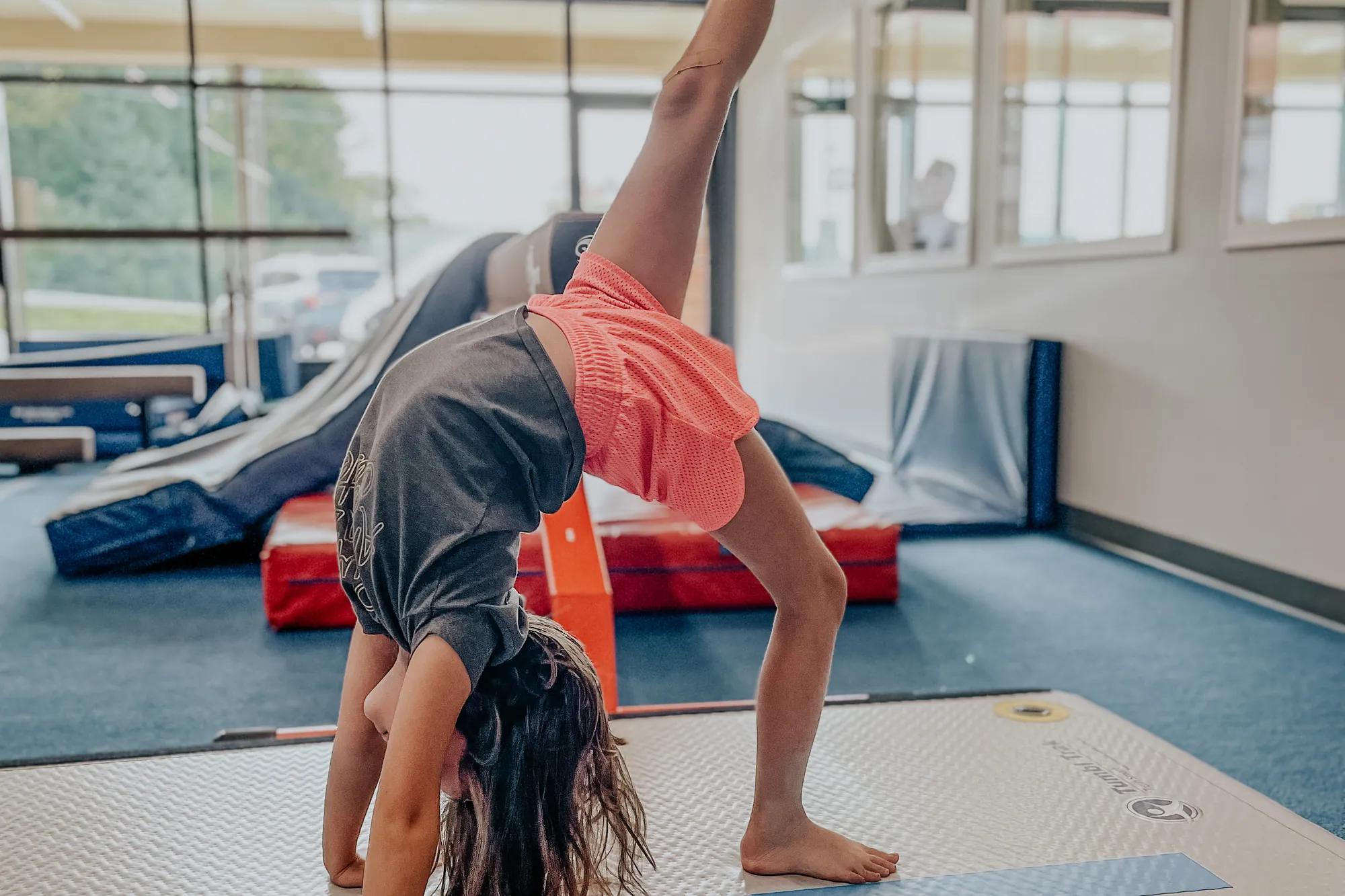 A girl in a backbend kicking one leg high on the tumbling floor