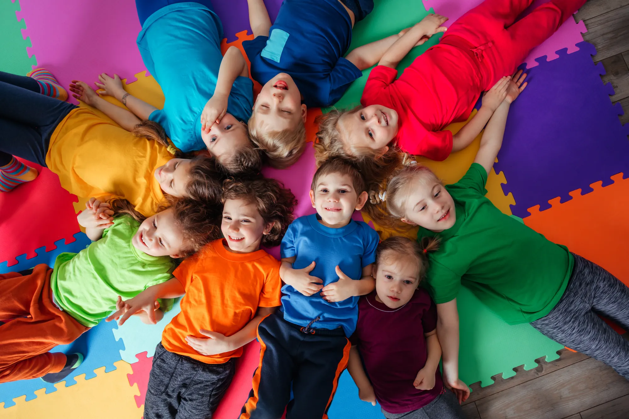 A group of kids in bright T-shirts lying in a circle on a colorful play mat