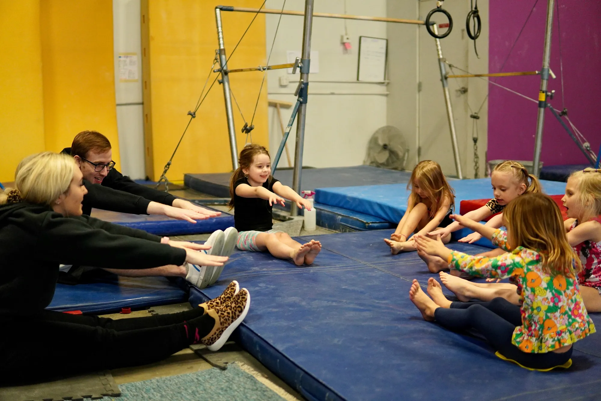 Kids and coaches stretching together on the floor of a bright gymnastics gym
