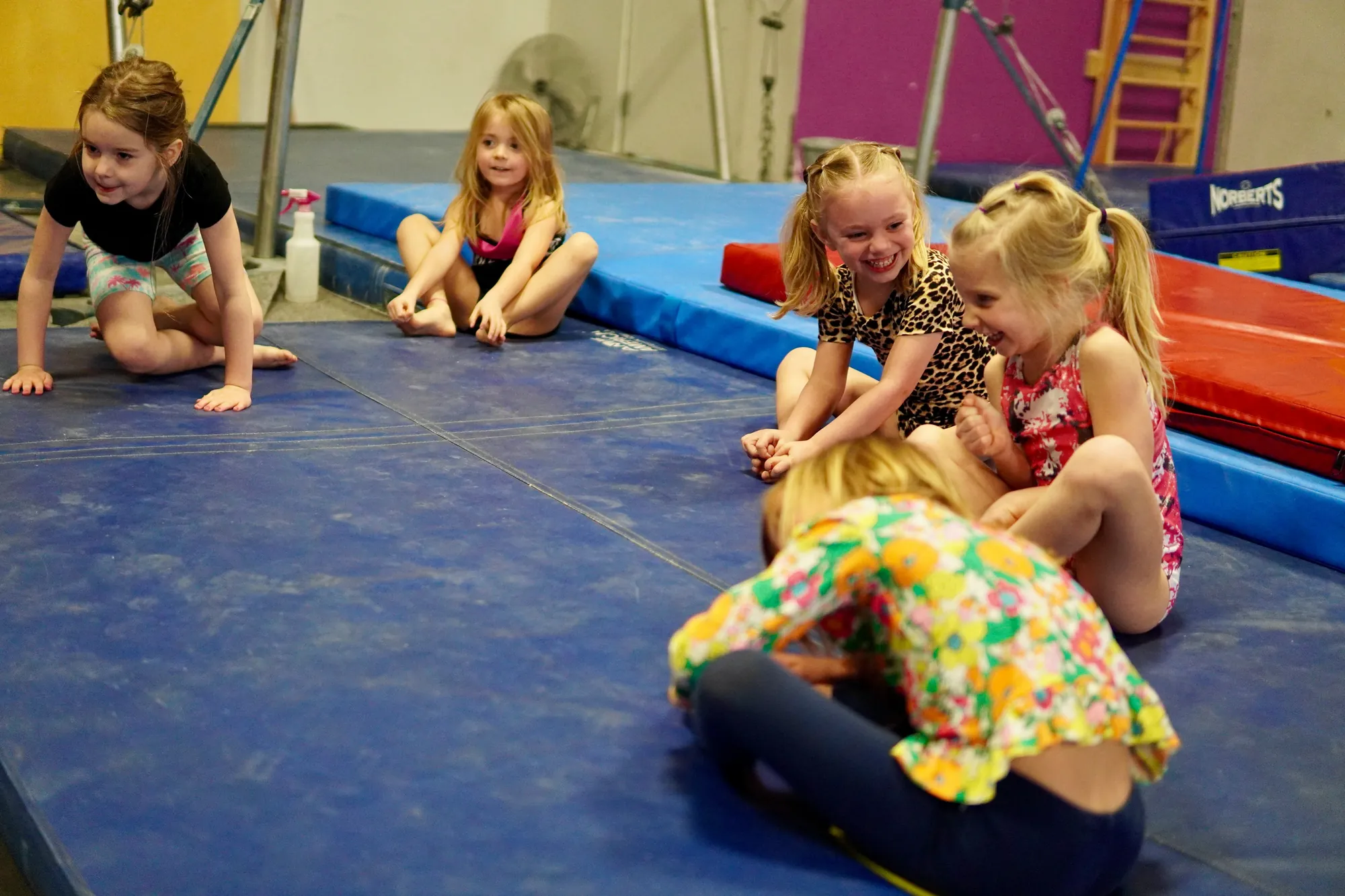 Young gymnasts laughing together on a blue gym mat