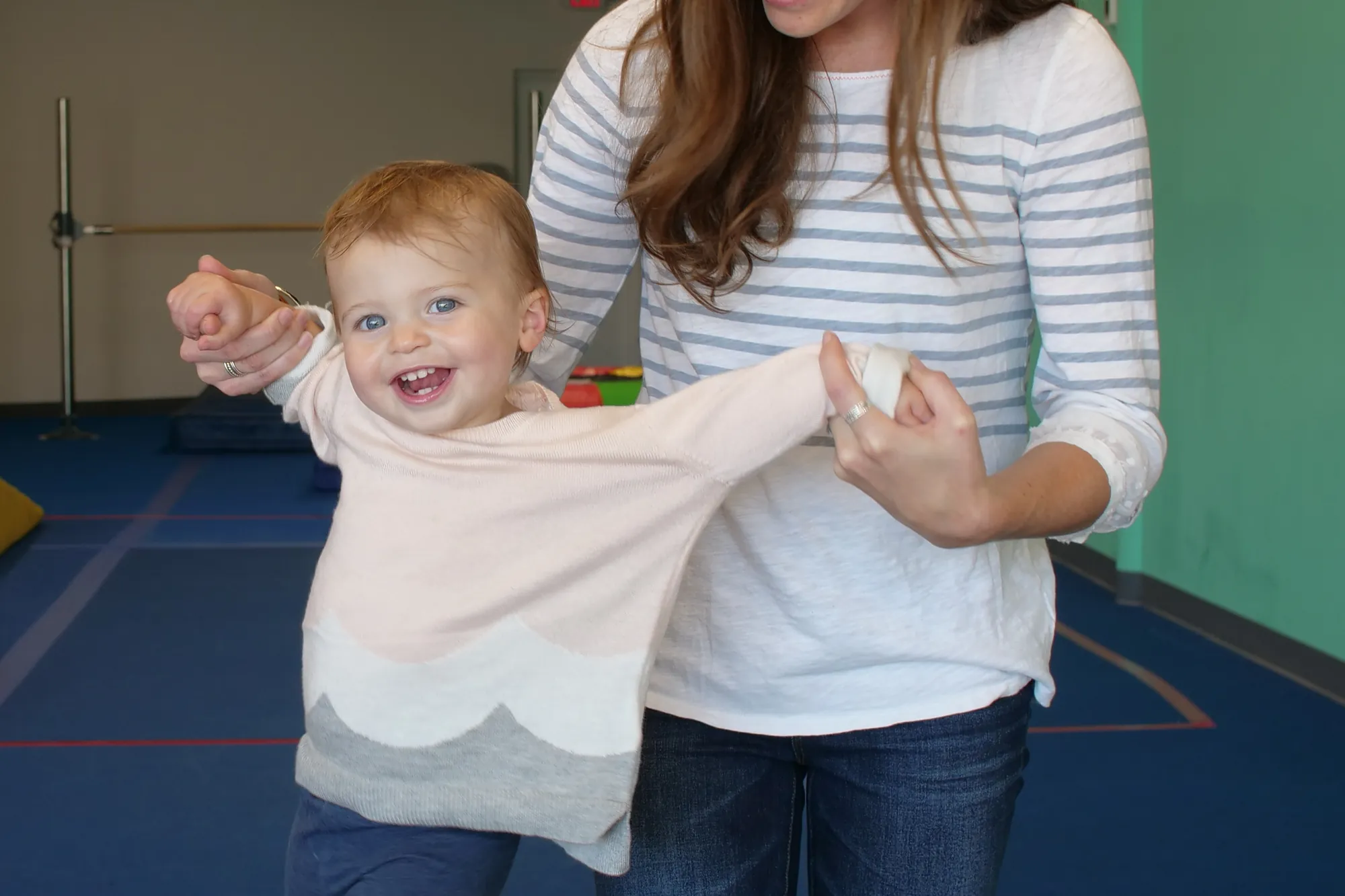 A mom holding her toddler's hands as she walks on the gym floor