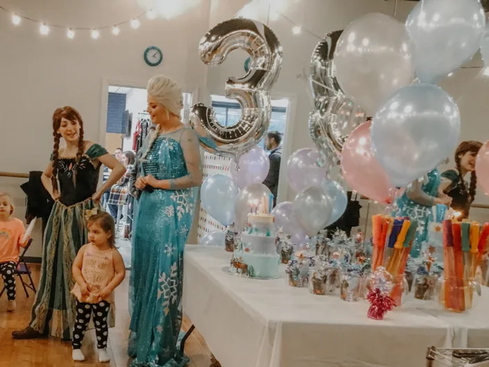 A princess character greeting kids at a balloon-filled party in the gym